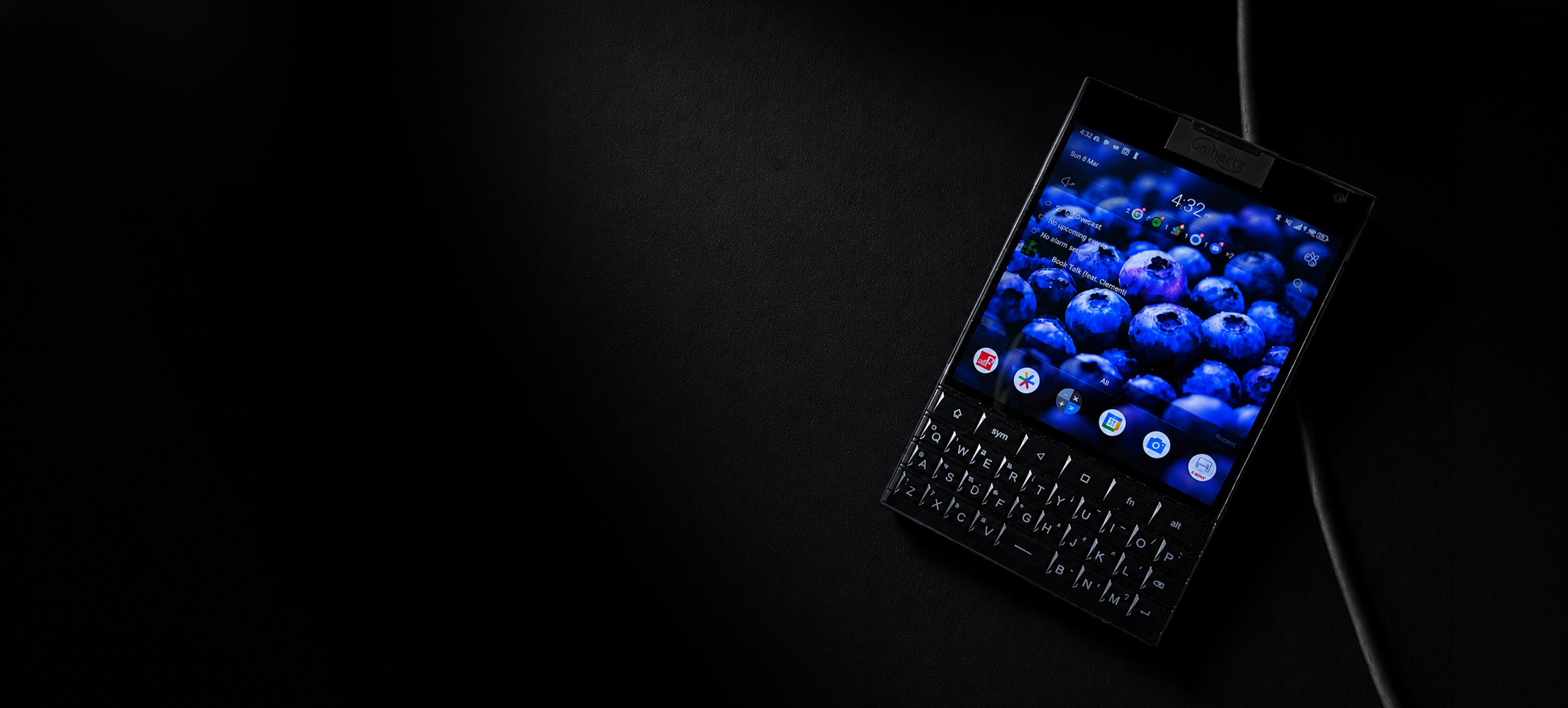 Ripe home screen with a blueberry wallpaper on a keyboard phone, lit against black.
